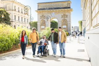 Groupe d'amis dont un fauteuil roulant devant l'arc de triomphe à Montpellier