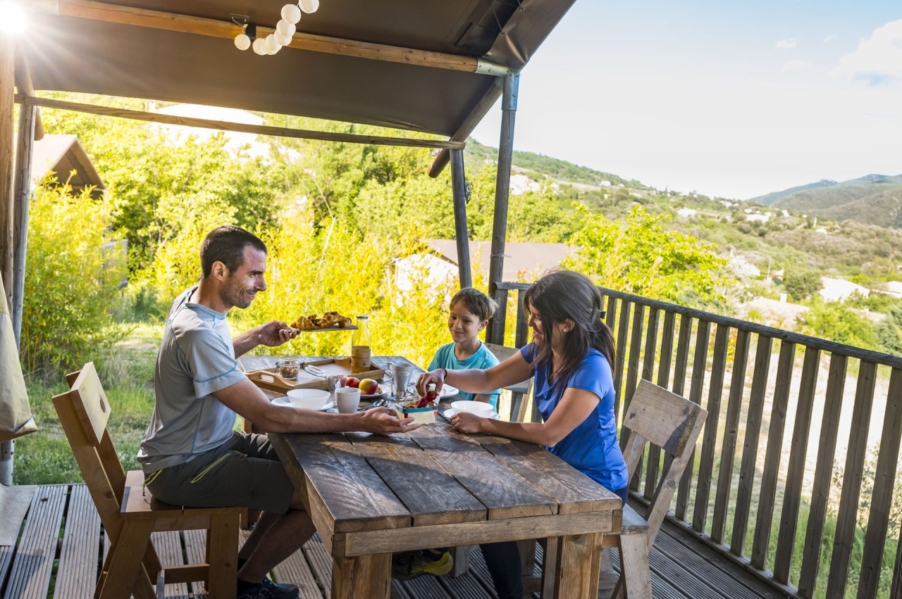 Une famille déjeune sur la terrasse d'une tente lodge au Camping du Caroux